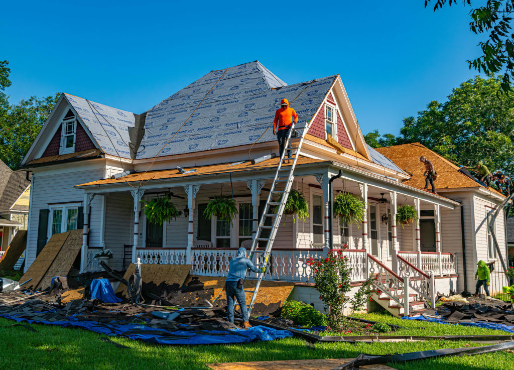 roofing crew installing new underlayment and shingles on a white residential house with a large porch