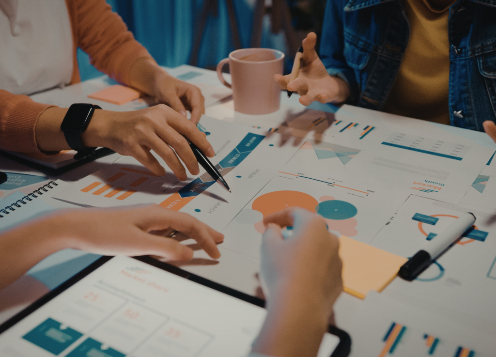 close-up of a diverse team collaborating on data charts, graphs, and marketing reports on a white desk with pens and sticky notes